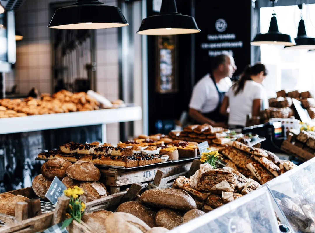 A bakery counter stacked with bread and pastries, two staff behind it
