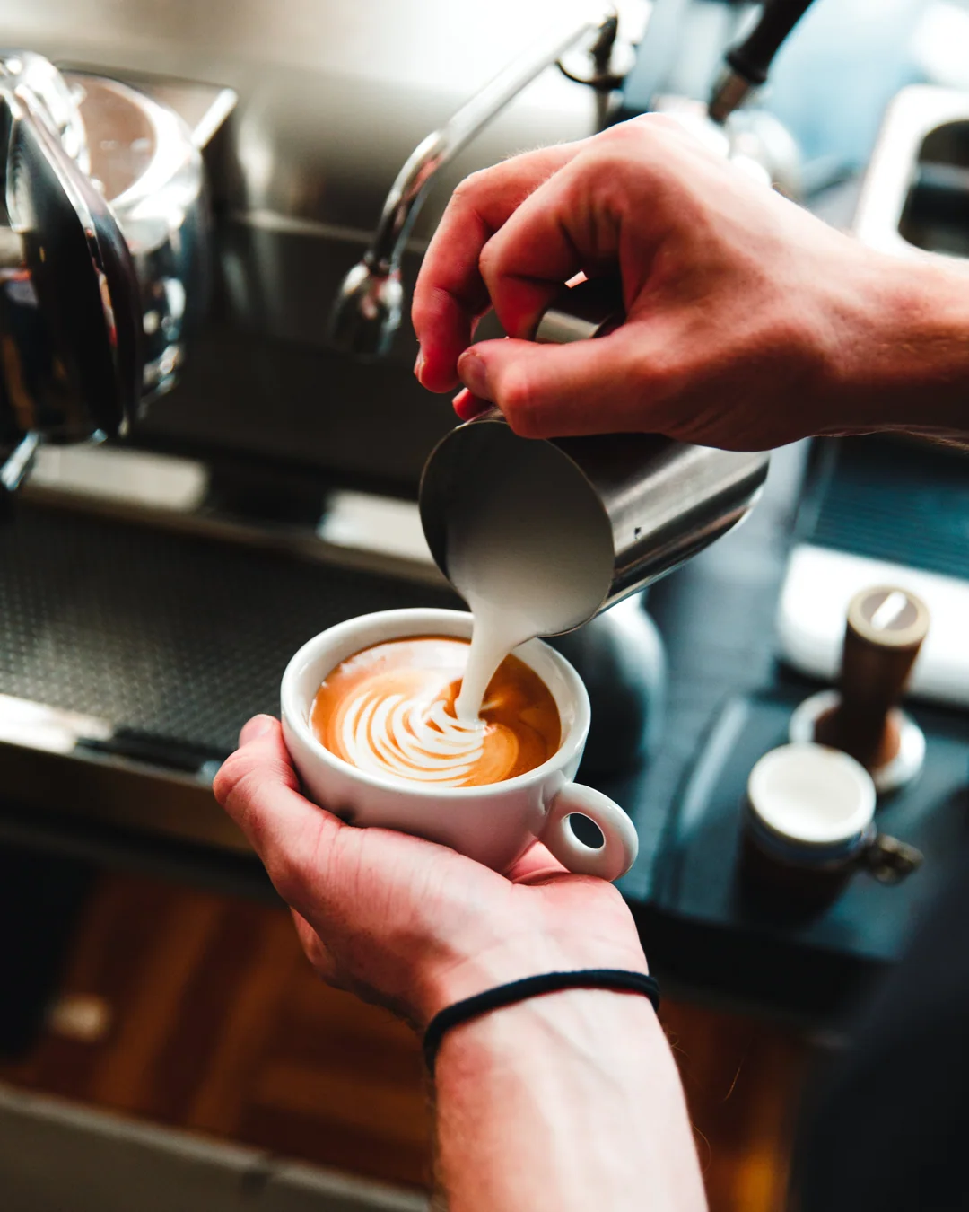 Un barista verse le lait dans un latte et dessine une feuille dans la mousse.