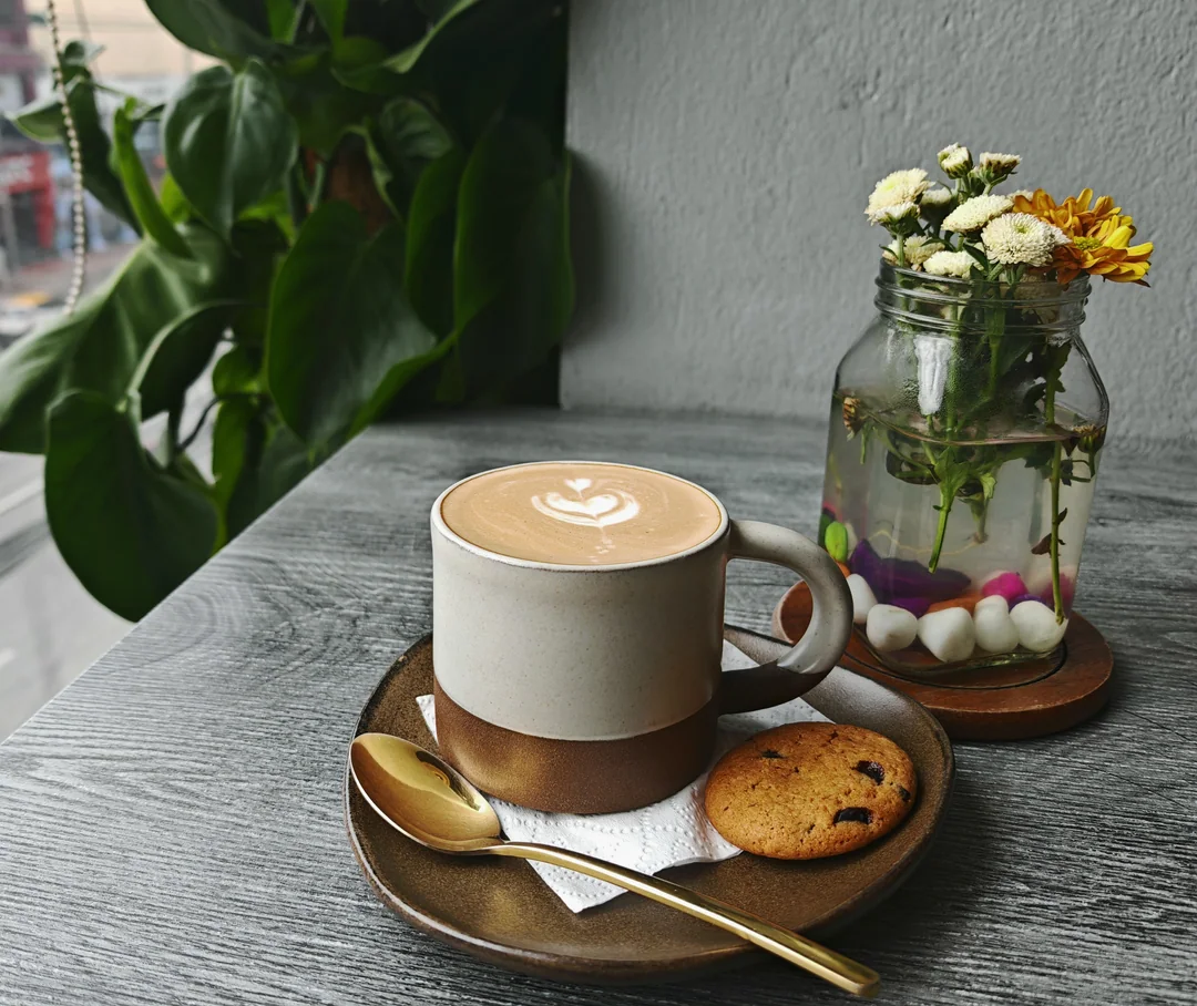 A cappuccino and a cookie on a café table, next to flowers