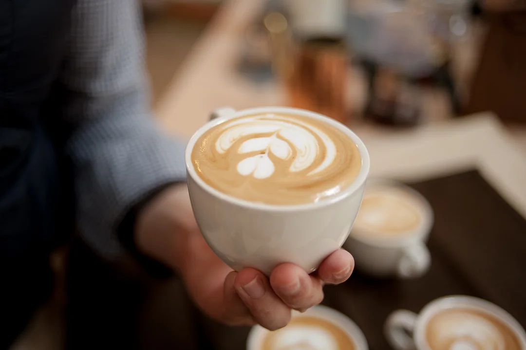 Deux tasses de café au lait décorées d’un cœur, tenues à la main au-dessus d’une table.