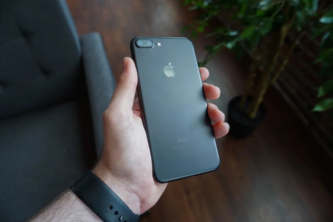 Une main tient un téléphone noir dans un salon.