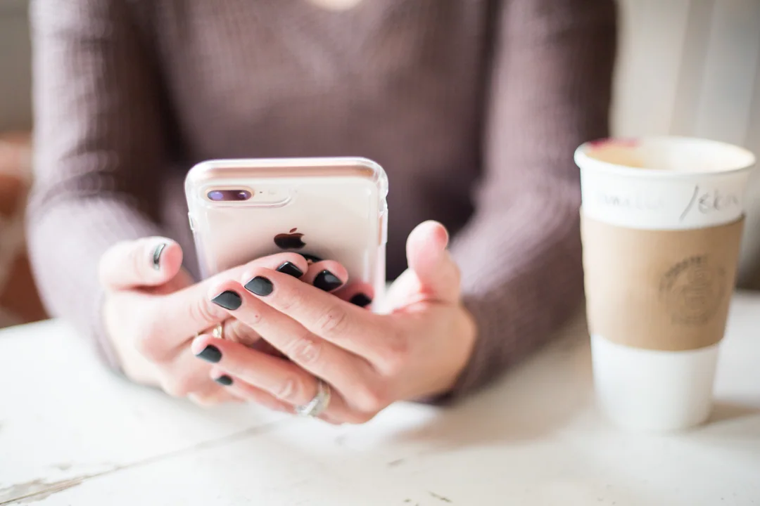 Two hands hold a phone above a table, a takeaway coffee beside it