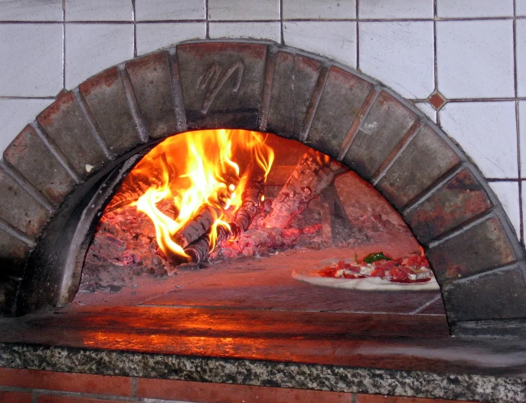 Un four à bois allumé, une pizza qui cuit près des flammes.