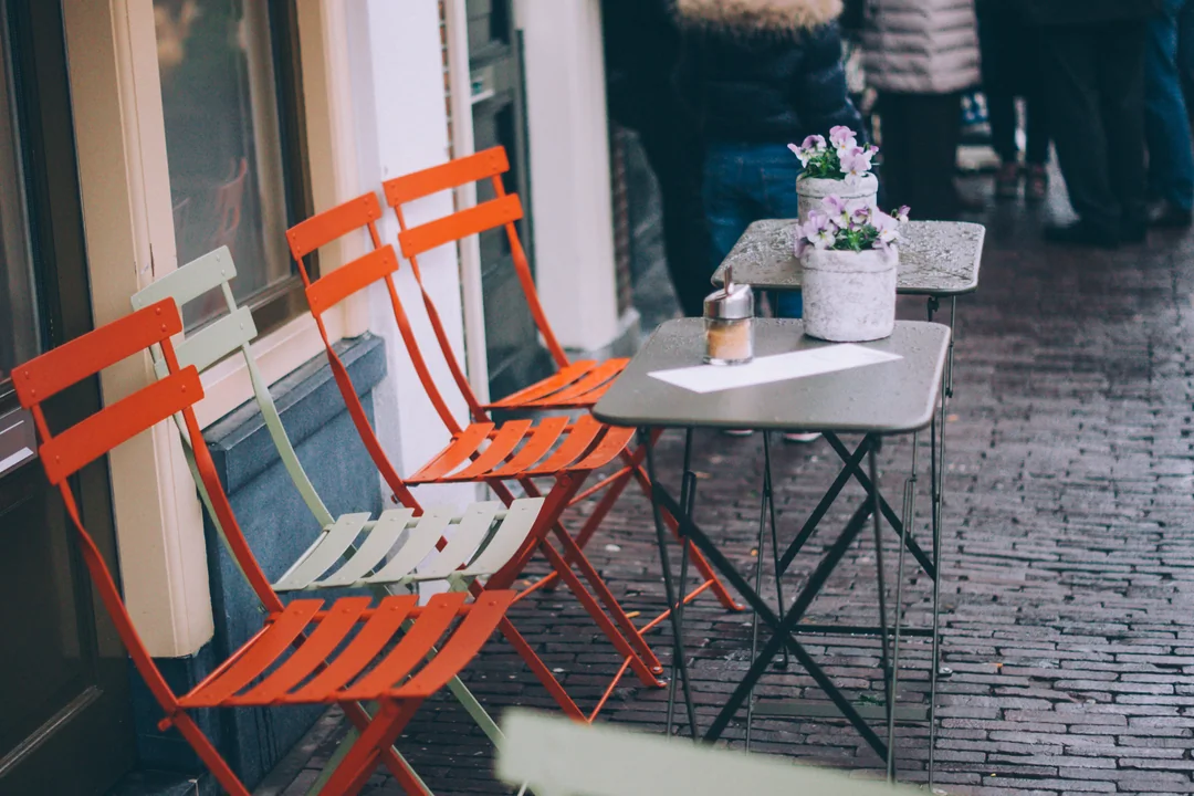Des chaises orange alignées sur la terrasse pavée d’un café.