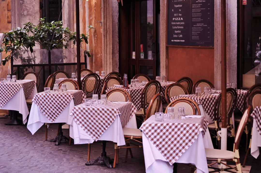 Tables with red and white checked tablecloths lined up on a trattoria terrace.