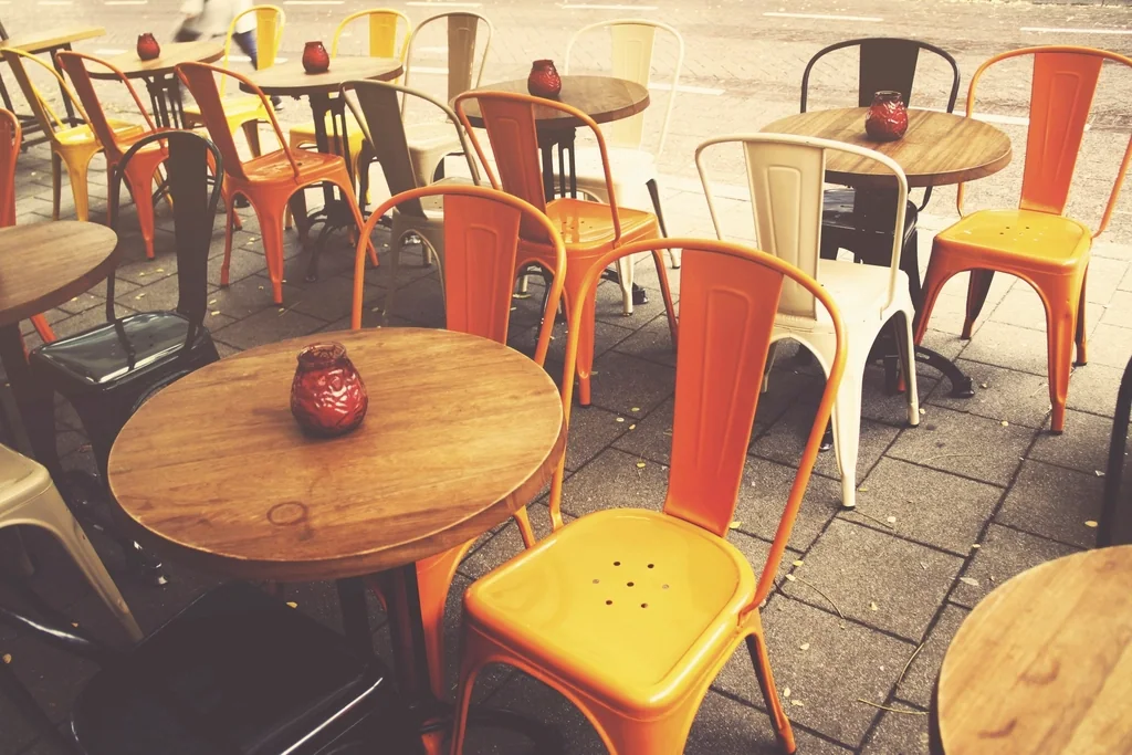 A café terrace, its round wooden tables and orange chairs lined up on the paving stones.